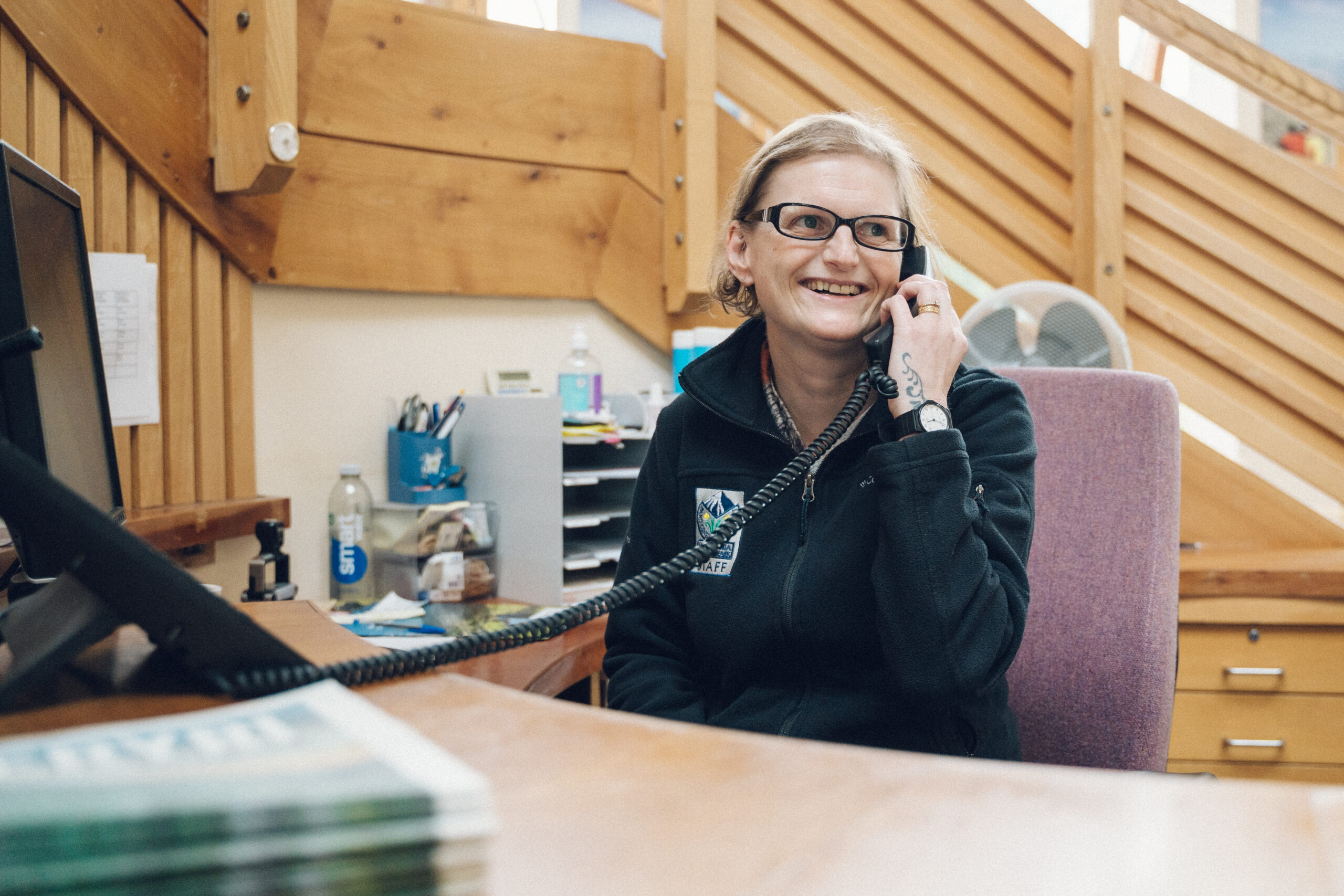 an image of a woman working in reception, with a wooden staircase in the back, smiling whilst answering the phone